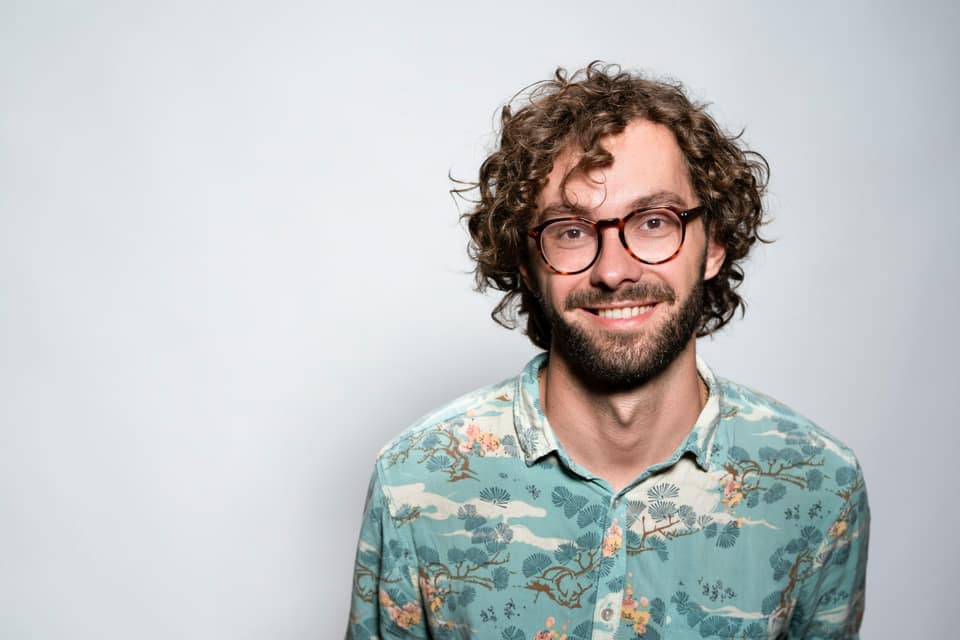 Lachende man met bril en krullen voor een lichte achtergrond